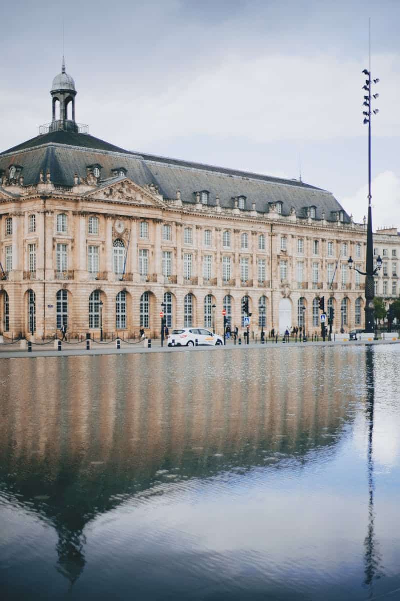 Elegant historic building in Bordeaux reflected in calm water, showcasing architecture.