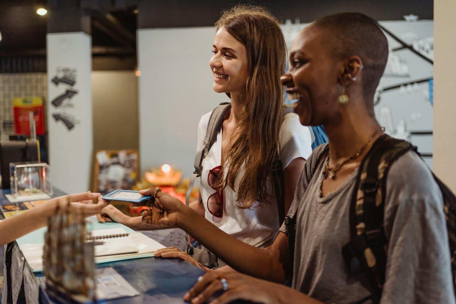 Two women enjoying a cheerful check-in at a hostel reception desk.